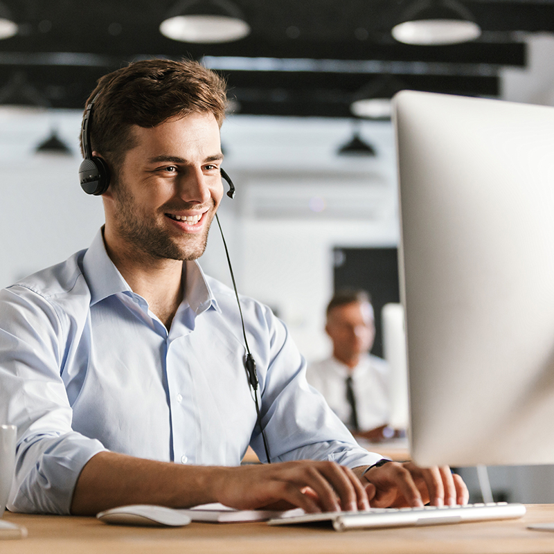 Mann mit Headset vor einem Bildschirm Ein Mann aus dem Notruf Service Center des Unternehmens ÖWD Security & Services mit Headset arbeitet lächelnd an einem Computer in einem Büro.